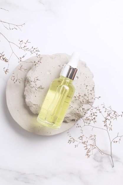 Cosmetic serum in glass bottle on stone podium Natural cosmetic product packaging design branding Marble background with flower branch