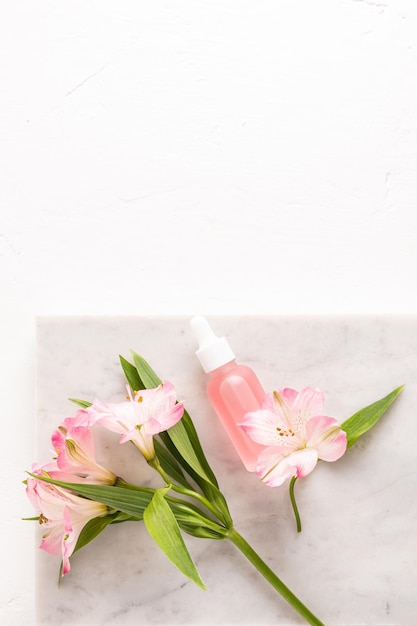 Cosmetic serum in a white matte bottle for face and body skin care lies on a white marble podium and a white background with a copy space