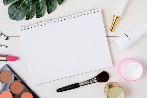 Cosmetic and skin care product and notebook on white wood table