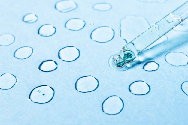 Cosmetic transparent drops on a blue background with a glass pipette