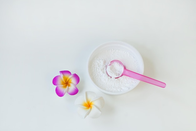 Cosmetic white powder with spoon in plastic container near frangipani flower or protein fine grains