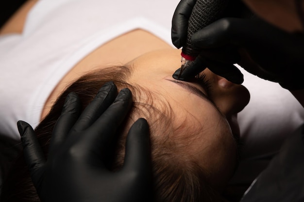 Cosmetician doing permanent brow tattoo to a woman