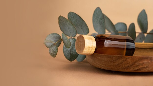 Cosmetics bottle from brown glass laying on the wooden plate with eucalyptus branch behind.Pastel background with fresh eucalyptus branch.Organic mockup concept,large banner.