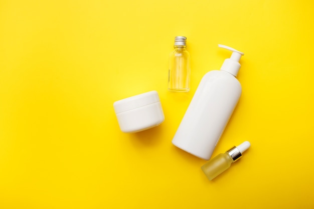 Cosmetics bottles on bright yellow background, top view, copy space. Mock up. White jars, bath accessories. Face and body care concept.