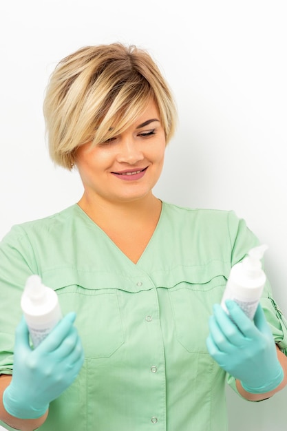 Cosmetics creams and skin care products in the hands of the female beautician smiling and standing over the white wall background