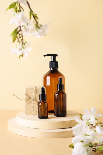 Cosmetics dark amber bottles with natural soap and spring flowers on wooden podium