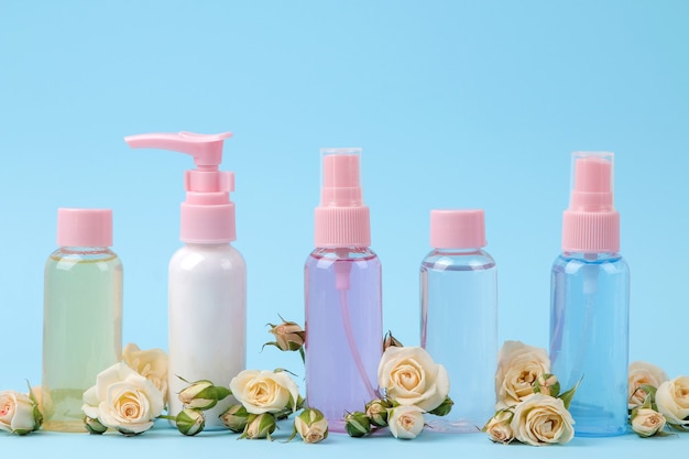 Cosmetics for face and body in pink bottles with fresh roses on a gentle blue background. creams and lotion. spa.