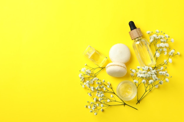 Cosmetics, macaroons and flowers on yellow background