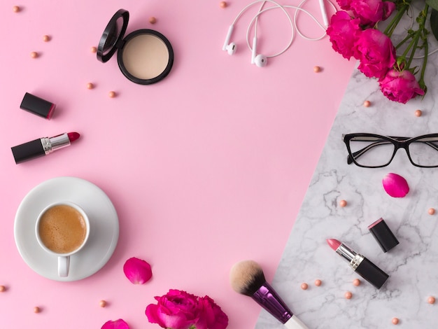 Cosmetics, makeup brushes, lipstick, powder and glasses with flowers on trendy pink marble 