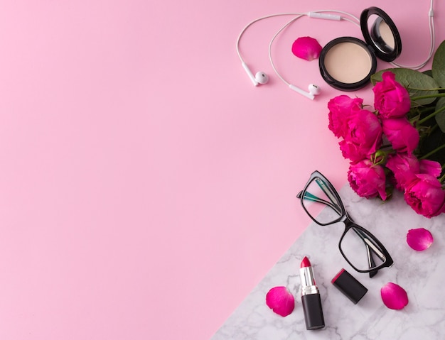 Cosmetics, makeup brushes, lipstick, powder and glasses with flowers on trendy pink marble 