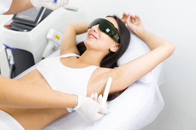 Cosmetologist applies gel for laser hair removal to woman armpit