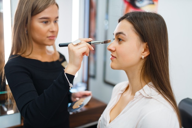 Cosmetologist applies makeup on a woman's face in cosmetics store. Luxury beauty shop salon, female customer and beautician in fashion market