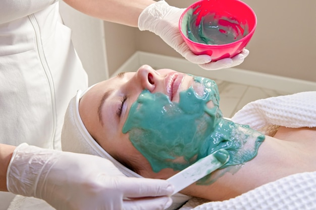 Cosmetologist applies a nourishing mask to a young woman in a spa salon