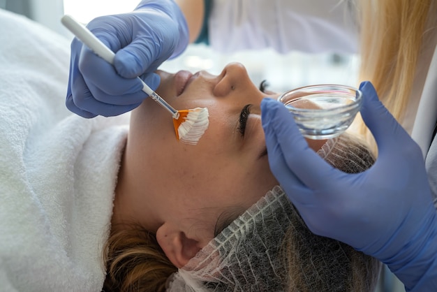 Cosmetologist applying healing cream on female client face skin in beauty clinic healthcare