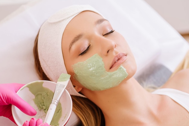 Cosmetologist applying mask on face of  woman in spa salon