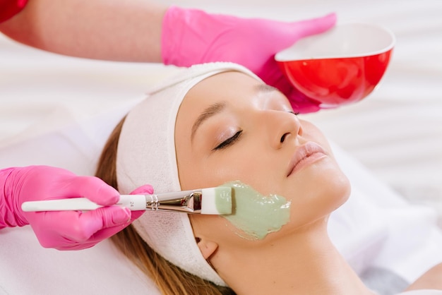 Cosmetologist applying mask on face of  woman in spa salon