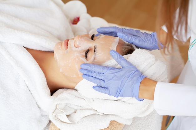 Cosmetologist applying sheet mask on woman in spa salon