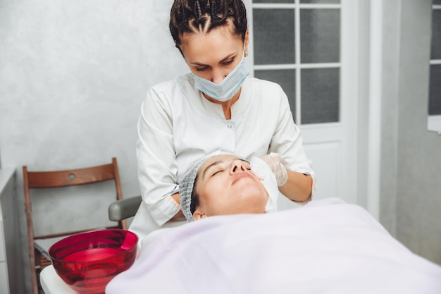 A cosmetologist cleanses the skin of a beauty salon client before the procedure and facial massage The concept of beauty and health cosmetology