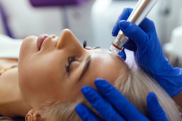 Cosmetologist doing anti aging procedure in cosmetology office he makes hydrafacial to a beautiful blonde woman