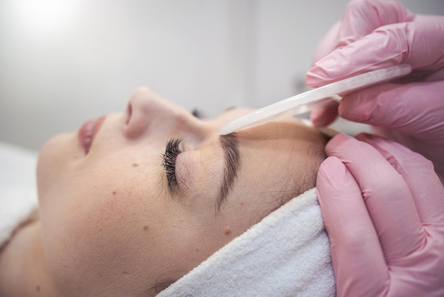 cosmetologist doing medical procedure with white gouache scraper on a client's face Health lifestyle