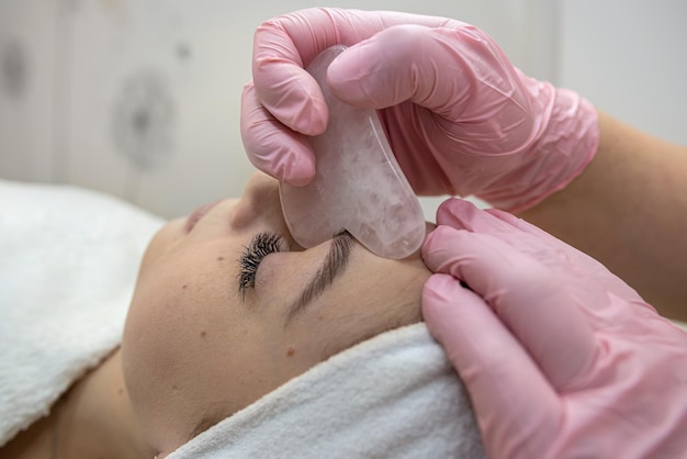 Cosmetologist doing medical procedure with white gouache scraper on a clients face