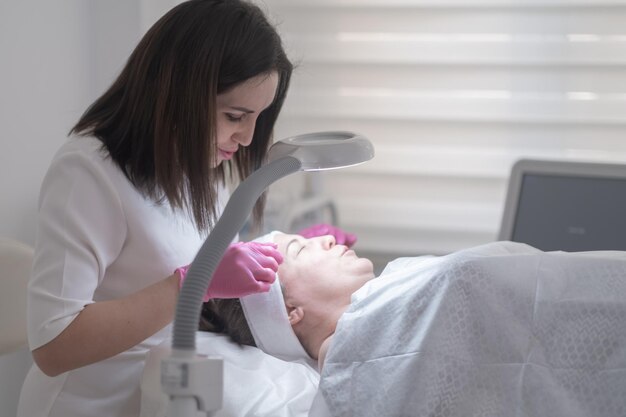 Cosmetologist examines a client39s skin through a magnifying lamp expertly curing any skin problems