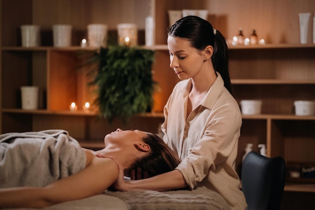 A cosmetologist girl does a facial and neck massage to a girl in the office for skin elasticity