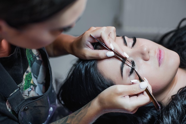 Cosmetologist hand does eyelash extension with eyelash brush close up