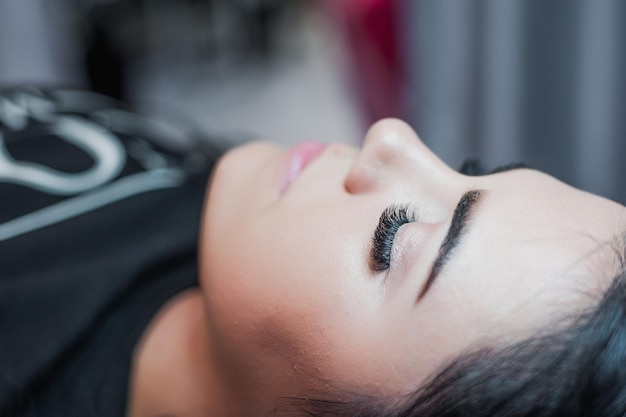 Cosmetologist hand does eyelash extension with eyelash brush close up