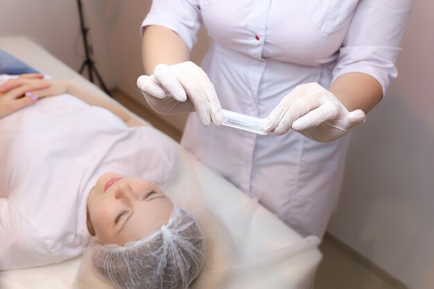 The cosmetologist holds a sterile bag with a needle in front of the client