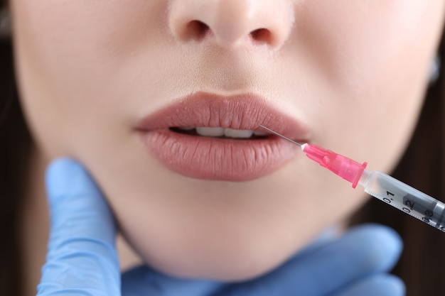 Cosmetologist makes injection to patient lips for augmentation