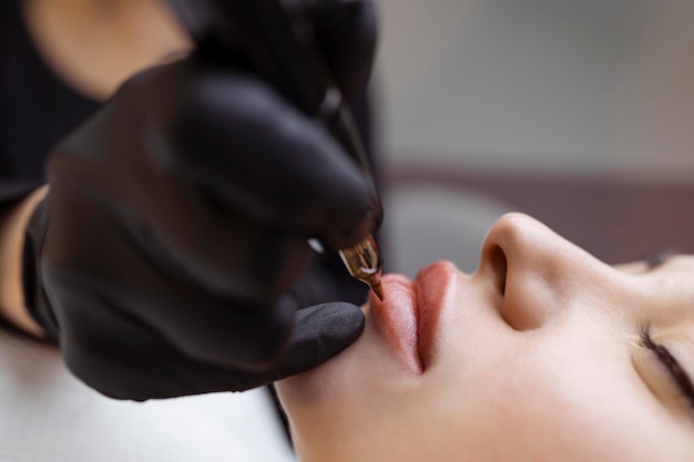 Cosmetologist makes permanent makeup on a woman39s face Specialist applies a tattoo on the patient39s lips closeup