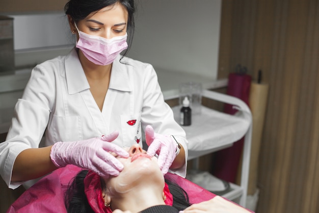 Cosmetologist making a face massage to her patient and a face mask. Anti-ageing procedure in a beauty salon.