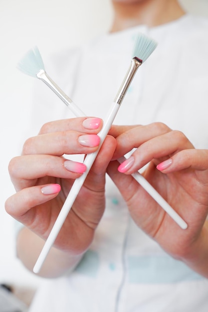 Cosmetologist in medical gear holding two cosmological brushes