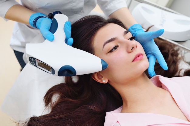 A cosmetologist performs a facial rejuvenation procedure for an attractive young girl using a special device-mesotherapy without injections and pain