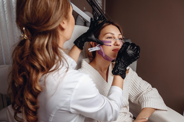 The cosmetologist performs a taping procedure to rejuvenate and improve the skin for a young female