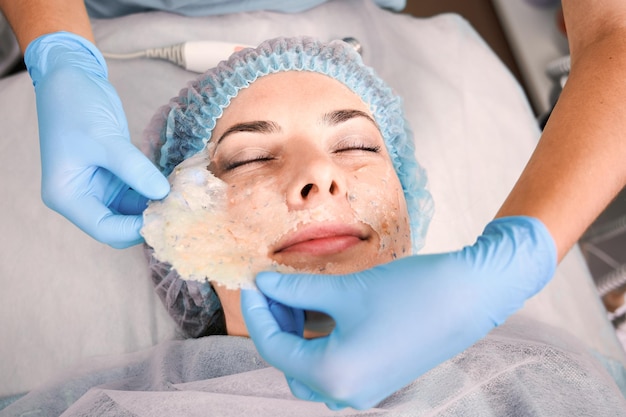 Cosmetologist removing cosmetic mask from woman face