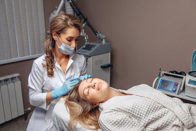 A cosmetologist specialist in a protective mask holds a syringe with an injection compound in his hands and prepares for the mesotherapy procedure