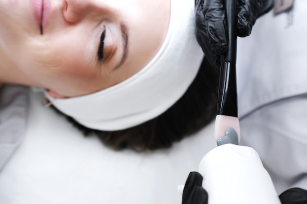 The cosmetologist squeezes a clay mask onto a brush and is about to apply it to the client's face