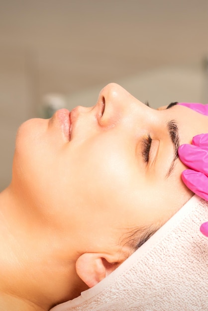 Cosmetologist with gloved hands applies a moisturizing mask with peeling cream on the female face Facial cosmetology treatment Procedures for facial care