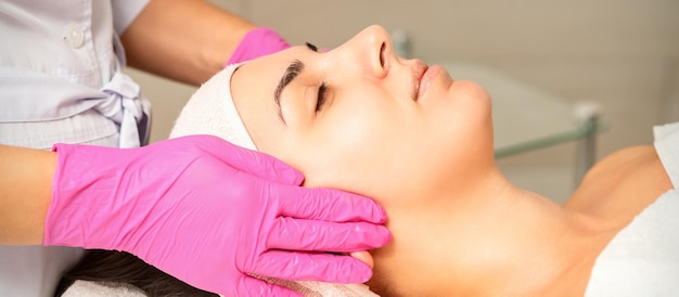 Cosmetologist with gloved hands applies a moisturizing mask with peeling cream on the female face Facial cosmetology treatment Procedures for facial care