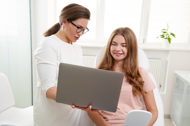 Cosmetologist working with patient while using laptop in clinic beauty doctor consults the patient