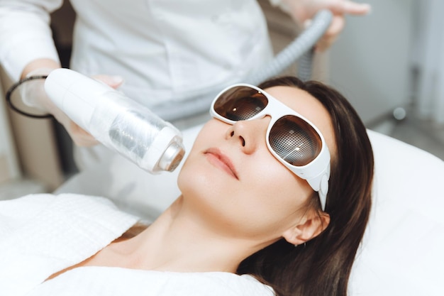 Cosmetology Beautiful woman getting laser hair removal procedure in beauty salon Closeup of a beautician's hands doing cosmetic procedures for a woman's face in a spa salon