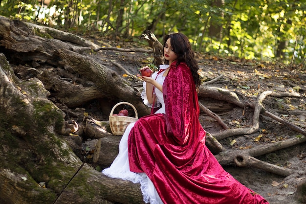 Cosplay to the fairy tale Snow White, a woman in a red cloak and a cart of apples in the woods