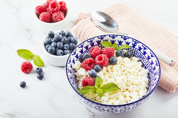 Cottage cheese in bowl decorated with raspberries and blueberries and mint leaves on white