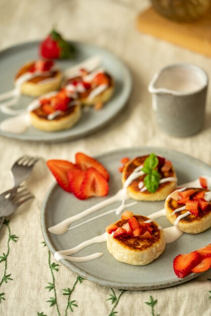 Cottage cheese cakes with strawberries and sour cream on plates breakfast table high quality photo top view