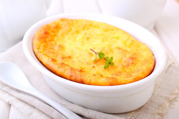 Cottage cheese casserole in white dish decorated with mint, on a white wooden background. Selective focus.