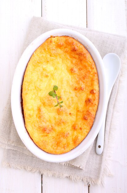 Cottage cheese casserole in white dish decorated with mint, on a white wooden background. Selective focus.