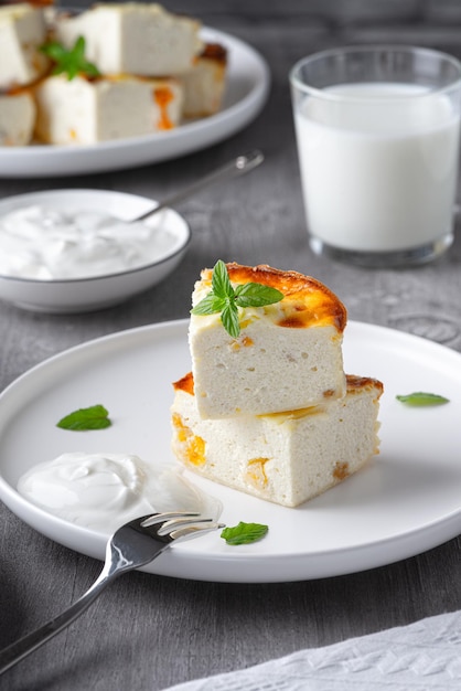 Cottage cheese casserole with raisins and cup of milk on wooden grey background