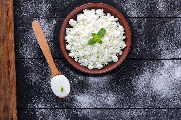 Cottage cheese in clay bowl on wooden boards Sour cream in wooden spoon Dairy products on dark background Copy space